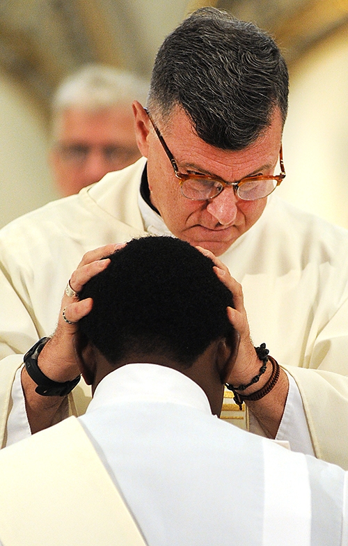 Father Joseph Rogliano, priest of St. Mark and St. Rose of Lima parishes, lays his hands on new priest Father Peter Nsa Bassey during a Mass at St. Joseph Cathedral. (Dan Cappellazzo/Staff Photographer)